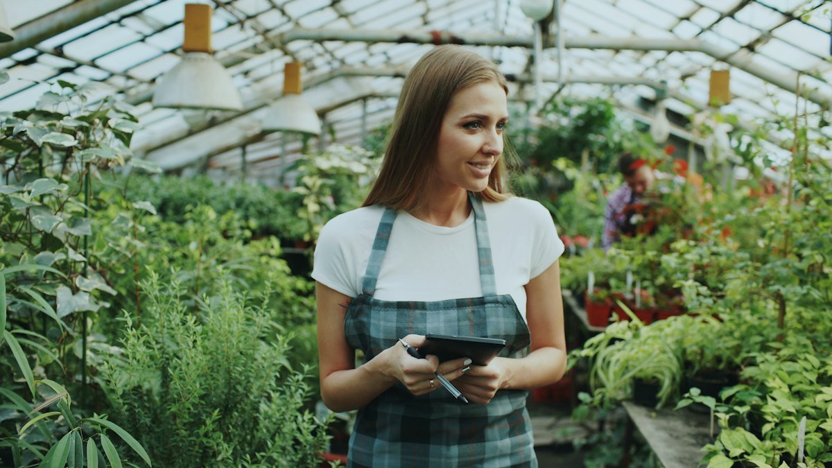 Mujer con una tableta trabajando en su vivero, entre plantas